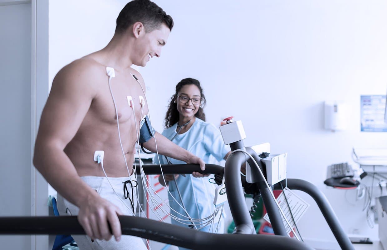 Patient on a treadmill during a cardiac stress test, monitored by a medical professional